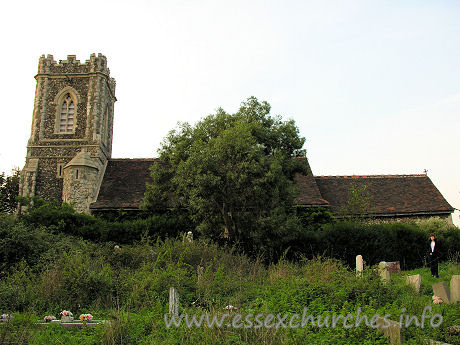 St James, West Tilbury Church – The S side of the church. The lovely Julie poses for us in front of the chancel. The churchyard, or, at least, the Church of England part of it, is in a rather dilapidated state. It is a shame, as there have been some recent (1997) burials here.