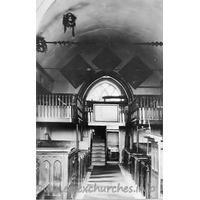 St Michael, Theydon Mount Church – Postcard 1: This black and white photograph is on display in the church. The West Gallery was built in 1837, during a restoration by Sir Edward Smyth, the then rector. The gallery was installed for use by servants and musicians. It was, however, removed in 1929, as it was in grave danger of collapsing. Suspended from the roof are two 'Coronals' or 'Maiden's Crowns'. These represent an old custom of placing such a crown on the coffin of a girl who had been betrothed, but had died before her marriage. They are shaped like a crown and are covered with evergreen leaves. There were originally three of these crowns in the church. Today there is just one remaining, though this is currently undergoing preservation and restoration. More details on this restoration can be found by clicking here.